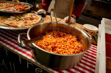 Büyük bir tencerede domates soslu İtalyan makarnası. Tepside pizza dilimleri.