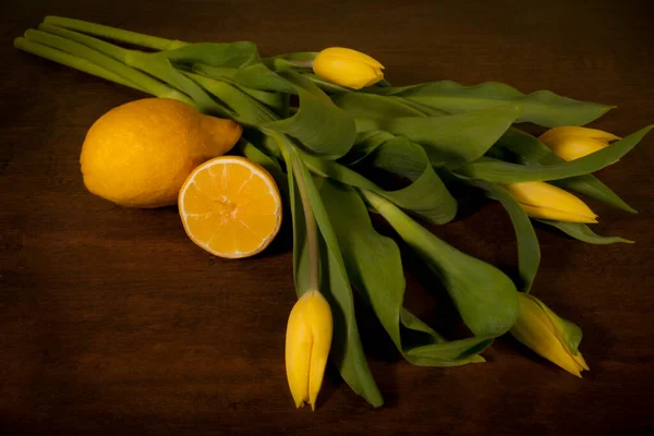 Stillleben. Gelbe Tulpen und Zitrone auf braunem Hintergrund. — Stockfoto