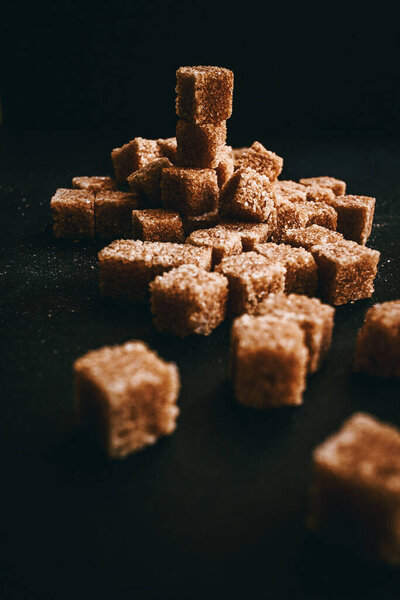 Brown cane sugar in cubes on a black background. Still life. 