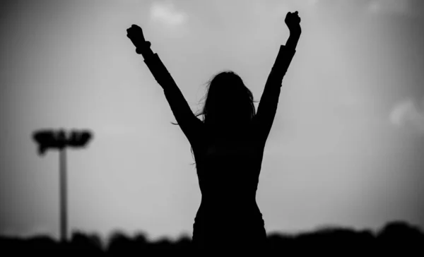 Black and white photography. Silhouette of a girl with raised hands on the football field. Victory