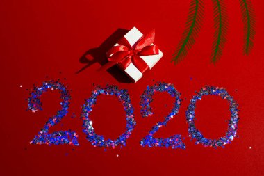 Kırmızı kurdeleli beyaz hediye kutusu, gelecek yılın figürleri, kırmızı arka planda yıldızlarla dolu.