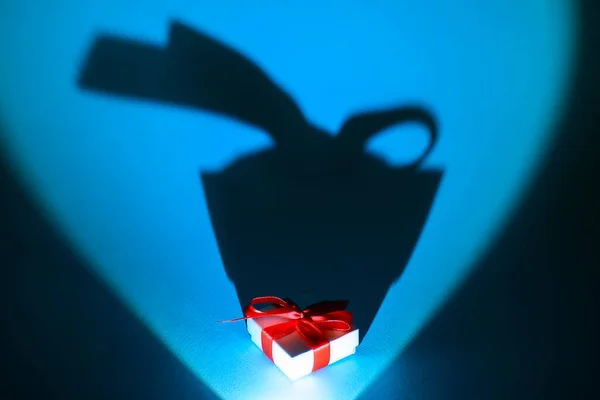 Weiße Schachtel mit einem Geschenk und einer Schleife auf blauem Hintergrund mit einem langen Schatten — Stockfoto