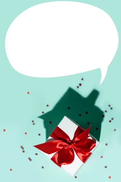 Caja de regalo blanca con una cinta roja y una dispersión de estrellas sobre fondo de menta. La sombra es como una casa . — Foto de Stock