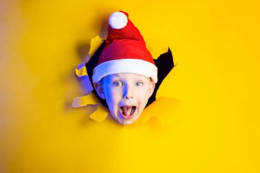 Küçük neşeli Noel Baba gülümsüyor, parlak ışıkla aydınlatılan sarı arka plandan çıkıyor.