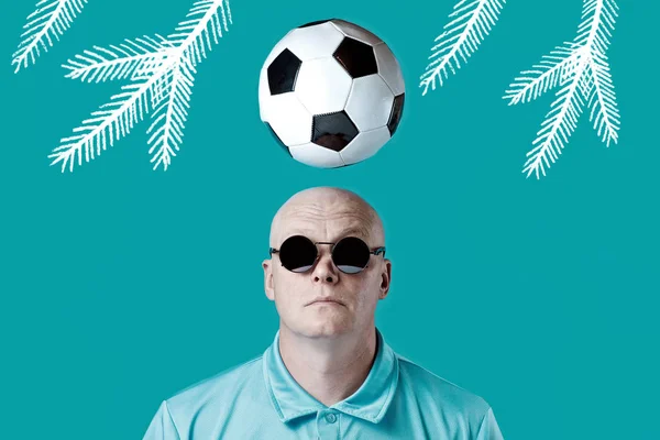 Calvo hombre brutal en gafas redondas oscuras con reflejos. Un balón de fútbol sobrevolaba. Sobre un fondo de menta . — Foto de Stock