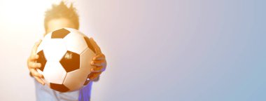 elinde bir futbol topu tutan mavi bir t-shirt çocuk mavi bir arka planda kafasını gizler