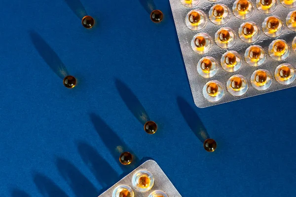 Una dispersione di vitamine olio di pesce e pacchetti con ombre. Sullo sfondo del colore dell'anno - classico blu . — Foto Stock