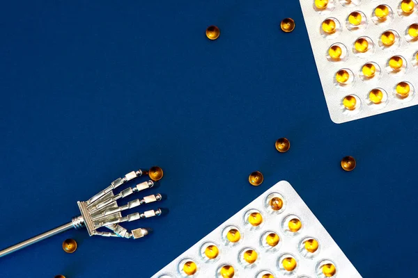 Robot arm and blisters with scattered vitamins with fish oil. Against a classic blue background. — 스톡 사진