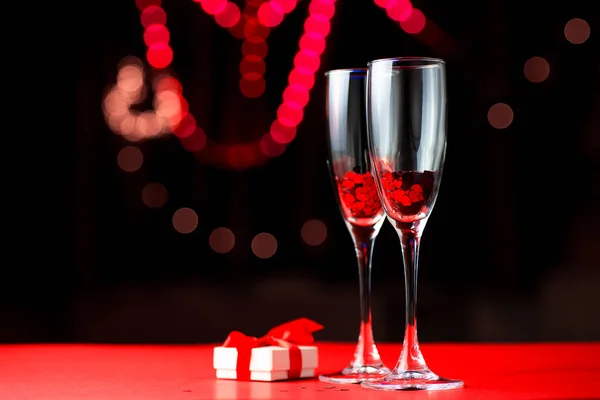 Two glasses of red hearts. Next to them lies a gift. Valentines Day abstract background. Blurred bokeh in the background. Valentines Day concept — Stock Photo, Image