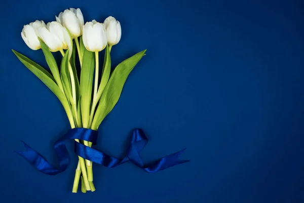 En buket hvide tulipaner bundet med et bånd. På en blå baggrund. Postkort til Valentinsdag og 8. marts - Stock-foto