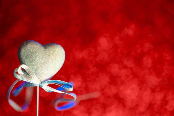 Un corazón con un arco. Rojo borroso bokeh en el fondo. El concepto para el Día de San Valentín — Foto de Stock