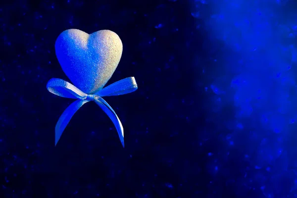 Un corazón con un arco. Azul borroso bokeh en el fondo. El concepto para el Día de San Valentín — Foto de Stock