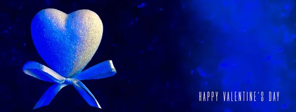 Μια καρδιά με τόξο. Μπλε θολή bokeh στο παρασκήνιο. Η ιδέα για την Ημέρα του Αγίου Βαλεντίνου — Φωτογραφία Αρχείου