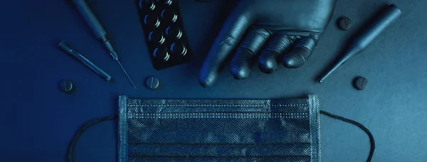 Virüsün düğmesi. Eldiven, maske, tablet, şırınga, şişeler koyu bir arka planda yatıyor. Pankart