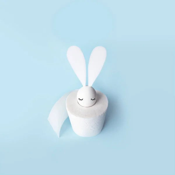 Bílé vejce se zajícovýma ušima v roli toaletního papíru. Tvrdý stín na světlém pozadí. Koncepce na Velikonoce 2020. — Stock fotografie