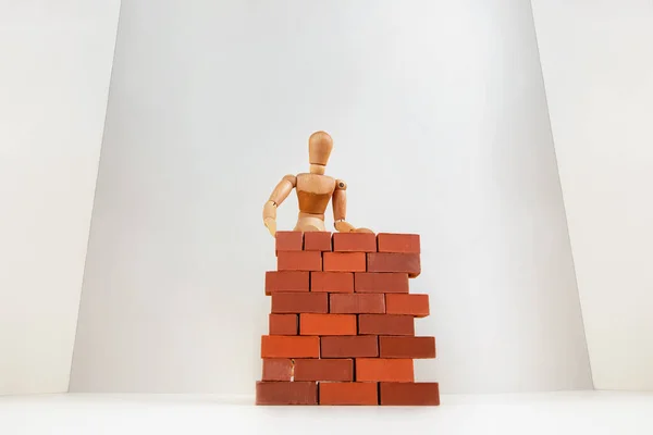 A wooden man builds a brick wall around him. Concept on self-isolation and coronavirus