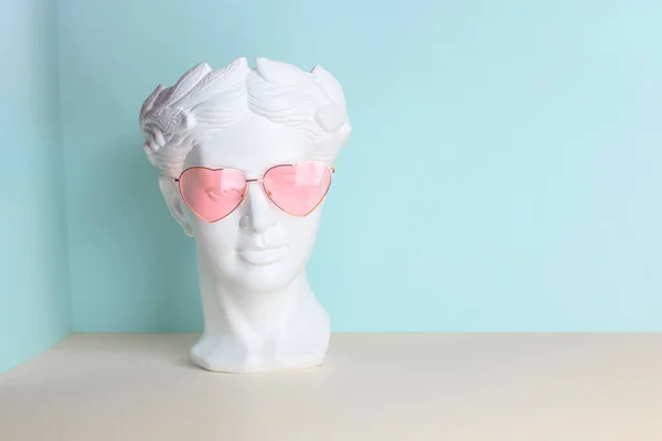 Hvid skulptur af et antikt hoved i lyserøde briller med hjerter. På en geometrisk baggrund af to farver. - Stock-foto