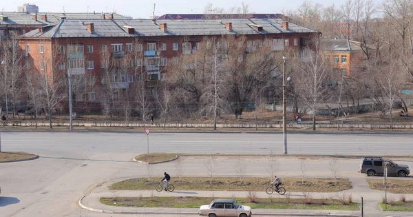 Paisagem urbana, casas de tijolos residenciais e estradas, pessoas mascaradas em bicicletas — Fotografia de Stock