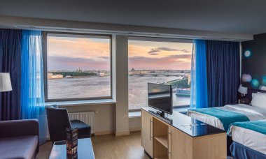Saint Petersburg, Russia - August 19 2018: Luxury modern interiors of hotel suite, floor to ceiling windows with beautiful aerial sunset view over Neva river and Saint Petersburg cityscape