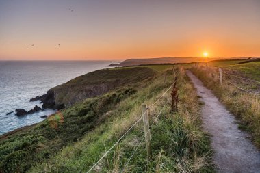 Güzel manzaralı gün batımı manzaralı Ballycotton uçurumu yürüyüşü, County Cork, İrlanda, alacakaranlıkta, sakin deniz, güneş batarken ufuk çizgisi, yalnız yol, popüler yürüyüş yolu, alacakaranlık, okyanus