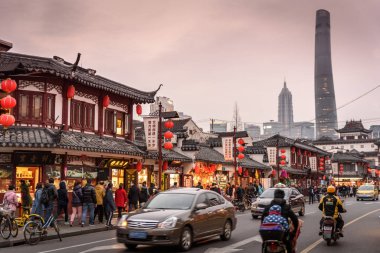 Shanghai, China - December 27 2017: Street scene in old town with traditional Asian buildings, people traffic cars motorbikes and Shanghai Tower skyscraper in the background. Cityscape photography