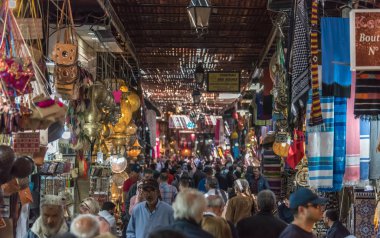 Marrakech, Morocco - April 2019: People and tourists walking along booths and stalls in alley nearby Jemma Dar Fna, the main souk market in Marrakesh medina, crowded bazaar