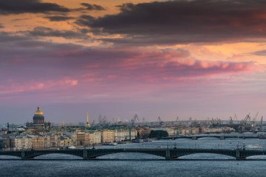 Beautiful summer aerial sunset view over Neva river and Saint Petersburg cityscape: Troitsky bridge, Winter Palace, Saint Isaac's Cathedral, and port cranes in the distance