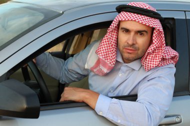 Kefiyeh giyen genç Müslüman adam arabada oturuyor.