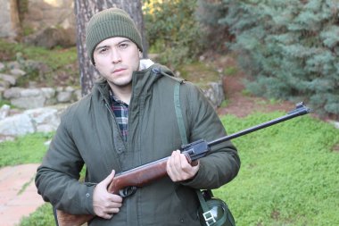 Ormanda tüfekle dikilen genç bir avcının açık hava portresi.