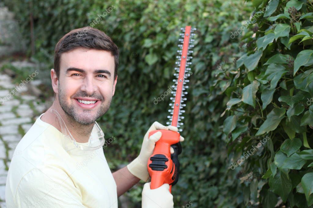 close-up portrait of handsome young man with electric saw cutting bushes in garden