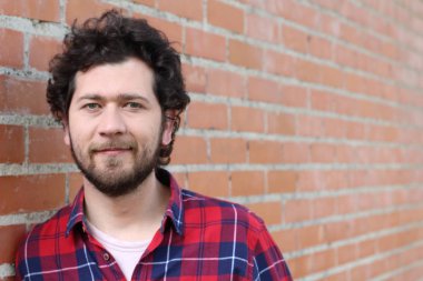 Duvarın önündeki kırmızı ekose gömlekli yakışıklı genç adamın yakın plan portresi.