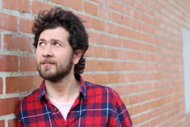 Duvarın önündeki kırmızı ekose gömlekli yakışıklı genç adamın yakın plan portresi.