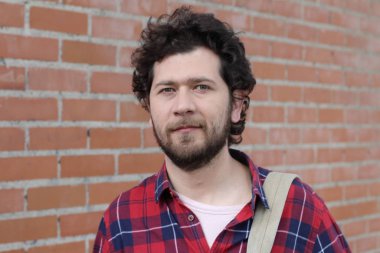 Duvarın önündeki kırmızı ekose gömlekli yakışıklı genç adamın yakın plan portresi.