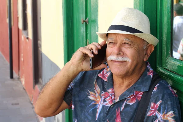 Tender senior man wearing hat using phone outdoors at daytime