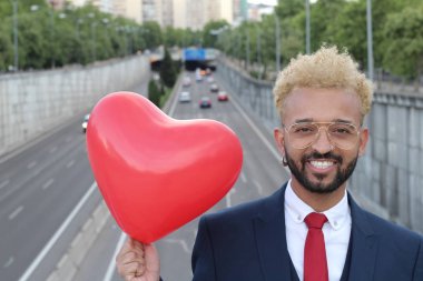 Sokakta kalp şeklinde balonu olan takım elbiseli yakışıklı bir gencin yakın plan portresi.