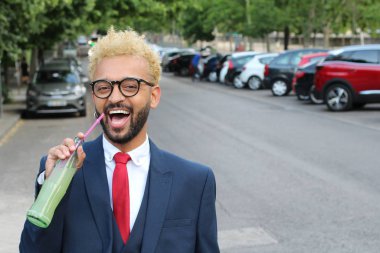 Takım elbiseli yakışıklı genç işadamının sokakta limonata şişesiyle yakın plan portresi.