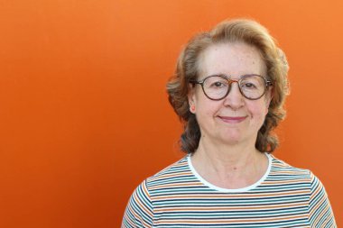 Stüdyoda poz veren gözlüklü gülümseyen yaşlı kadının portresi.