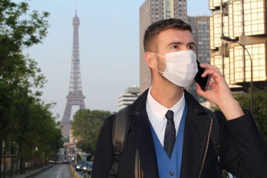 Gündüz vakti Paris caddesinde dikilen günlük giysiler ve maske giyen klasik görünümlü bir beyefendi.