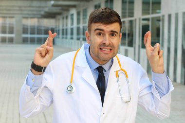 Steteskop parmaklarını çaprazlayan ceketli yakışıklı genç doktorun yakın plan portresi.