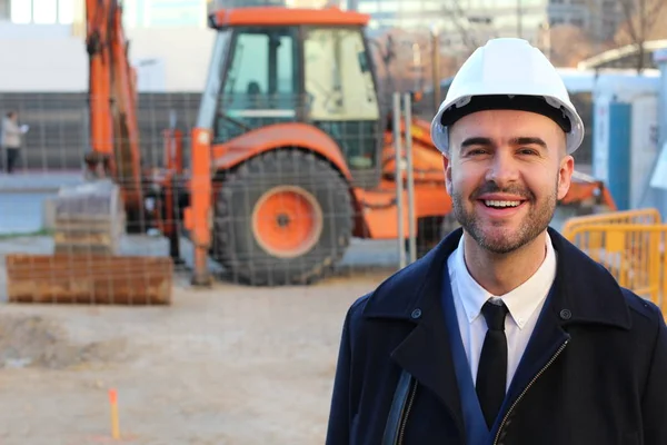 Young businessman in helmet on construction background with blurred tractor