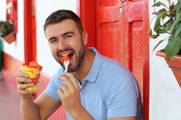 路上でプラスチック製のカップから果物を食べるハンサムな若い男のクローズアップ肖像画 — ストック写真