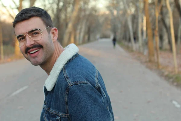秋の公園でデニムジャケットと眼鏡を身に着けている口ひげを持つ若い男 — ストック写真