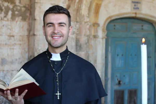 Smiling priest holding open bible on church background