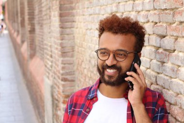 Ekose gömlekli yakışıklı genç adamın yakın plan portresi tuğla duvarın önünde telefonla konuşuyor.