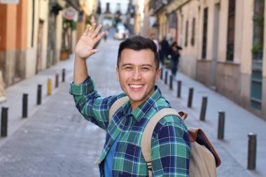 Ekose gömlekli yakışıklı genç adamın yakın plan portresi. Sokakta kameraya el sallıyor.