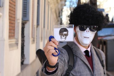 Kafatası maskeli ve peruklu yakışıklı genç adamın yakın plan portresi.