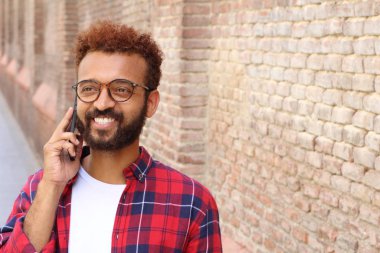 Ekose gömlekli yakışıklı genç adamın yakın plan portresi tuğla duvarın önünde telefonla konuşuyor.