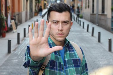Ekose gömlekli yakışıklı genç adamın yakın plan portresi sokakta dur işareti gösteriyor.