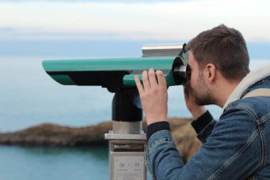 Deniz kıyısındaki dürbünlere bakan yakışıklı genç adamın yakın plan portresi.