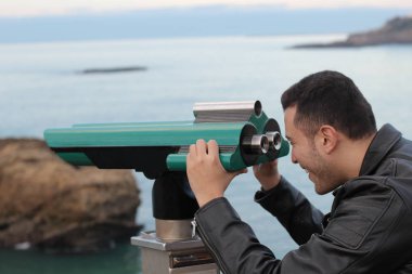 Deniz kıyısındaki dürbünlere bakan yakışıklı genç adamın yakın plan portresi.